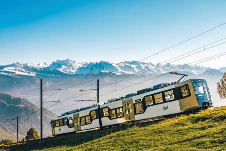 Rigi cogwheel train ascending through lush landscapes with stunning views of the Swiss Alps in the backdrop.