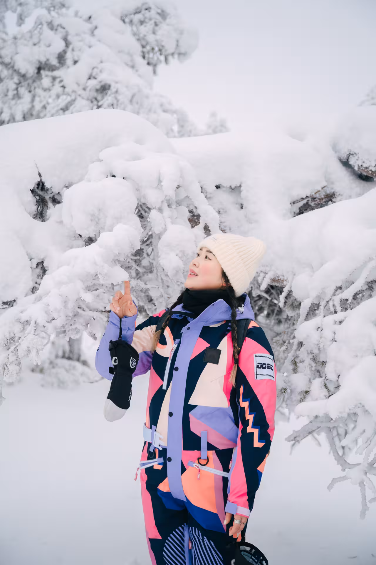 Woman in vibrant winter gear admiring snow-laden branches during Riisitunturi winter photography hike.