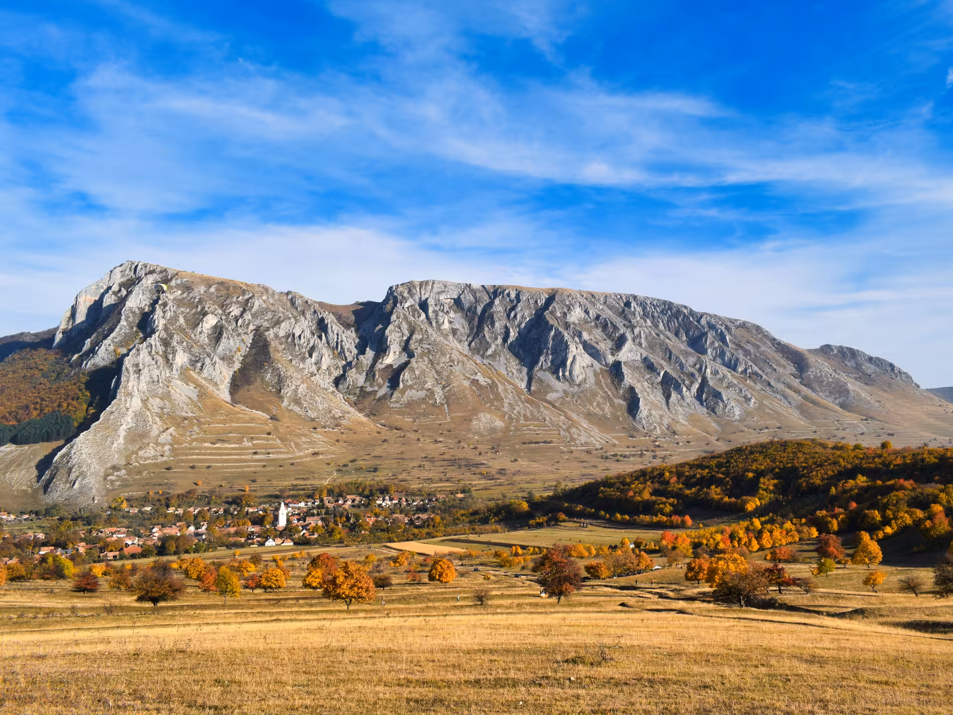 Panoramic autumn view of Rimetea village nestled below dramatic Apuseni Mountains rocky limestone peaks Romania