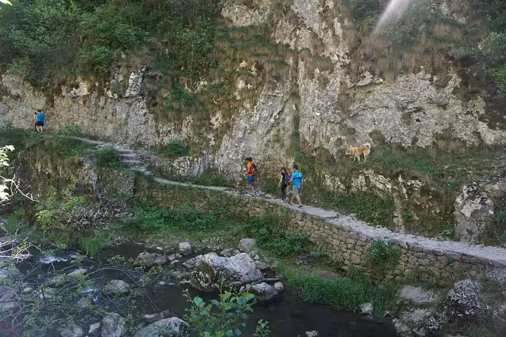 Hikers and dog walking along stone path beside rocky cliff and river in Rimetea area, Romania