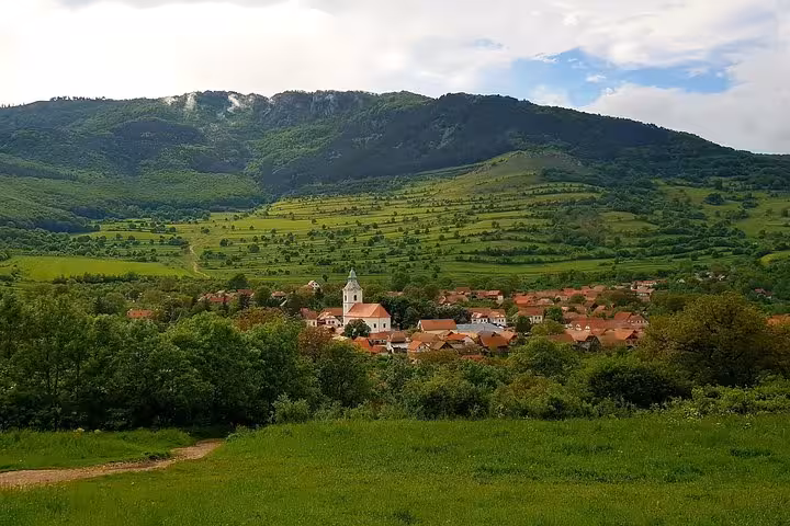 Panoramic view of Rimetea village with church steeple, red-roofed houses, and green mountains in Transylvania