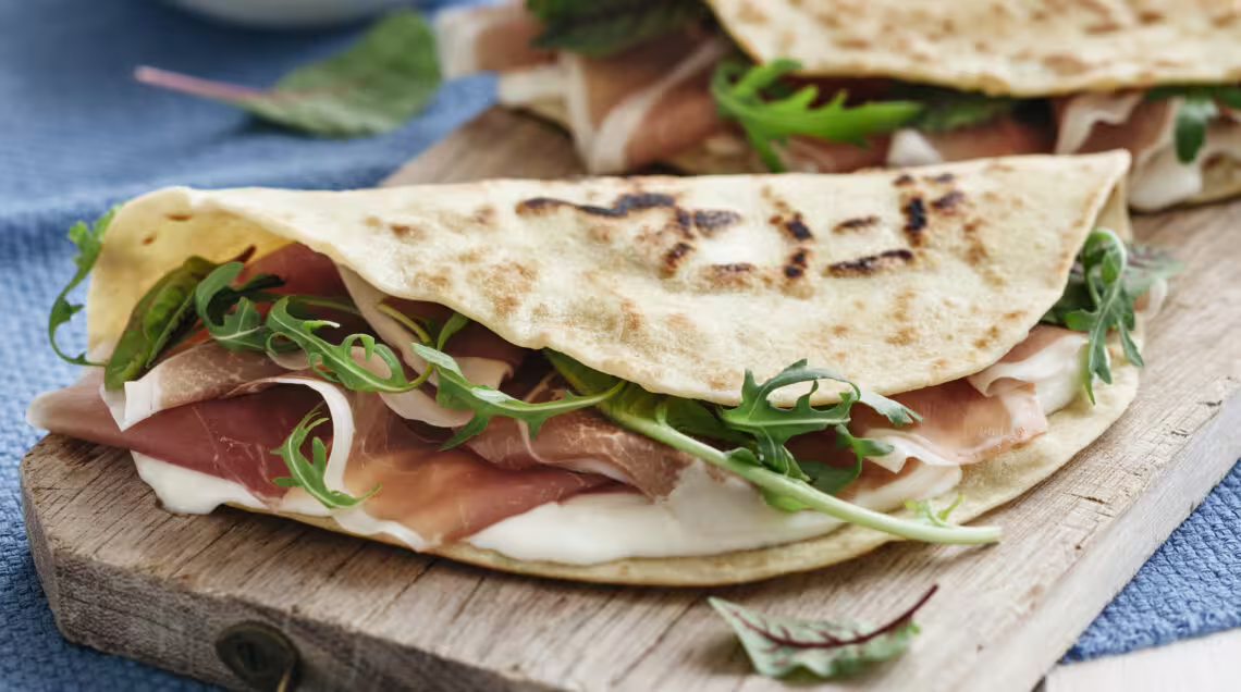 Close-up of classic Rimini piadina with prosciutto crudo, stracchino and rocket on a rustic board