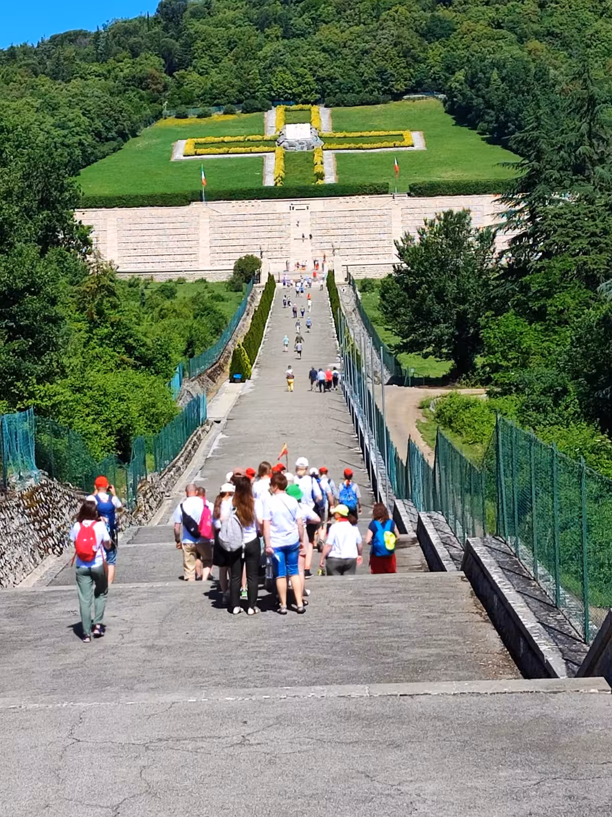 Visitors walking up a scenic path towards a beautifully landscaped cross monument on L'Anello della Collina Imprendibile.