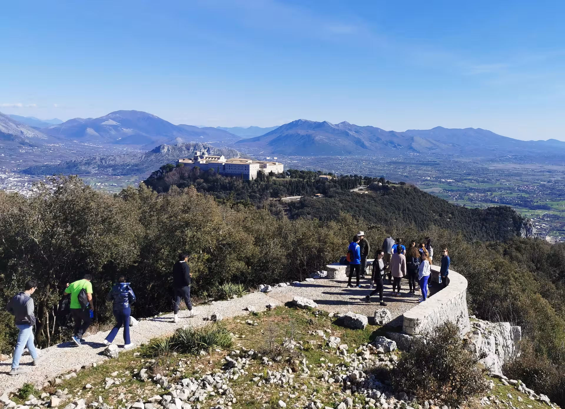 Tourists enjoy panoramic views of historic monastery and mountains on L'Anello della Collina Imprendibile hike.