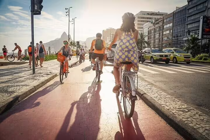 Group of cyclists pedals along Rio's vibrant beachfront promenade at sunset, highlighting urban and natural beauty.