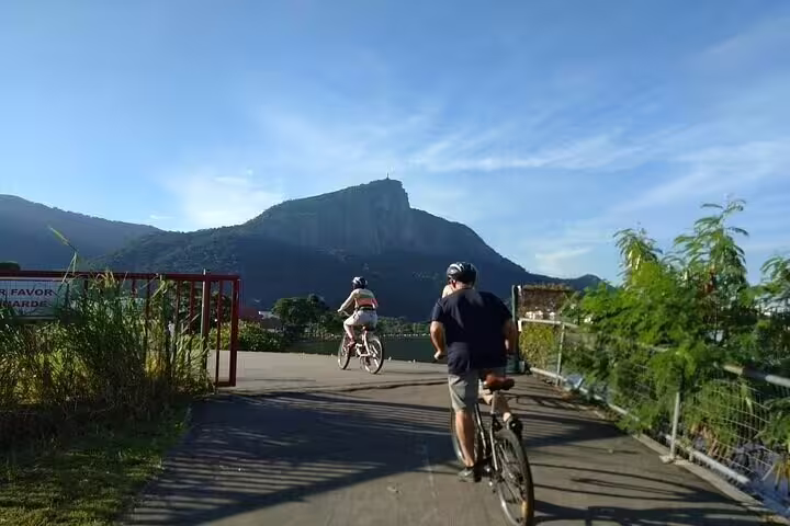 Cyclists ride towards iconic mountain landscape under a clear blue sky on Rio's scenic bike path.