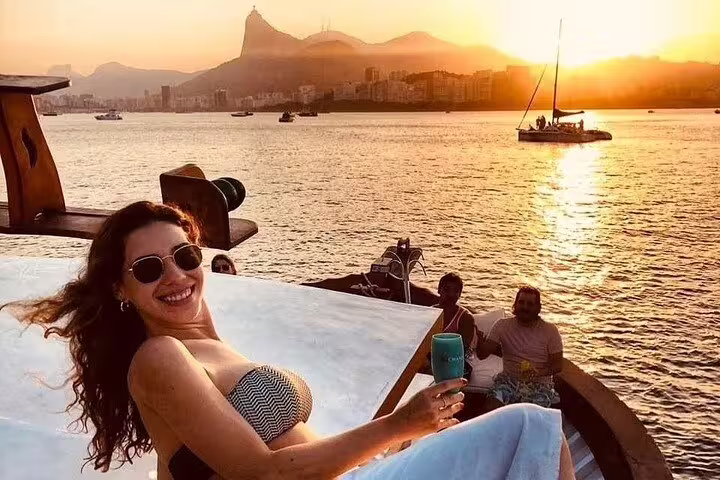 Woman relaxing with a drink on a boat at sunset in Rio, overlooking scenic city views and Sugarloaf Mountain.