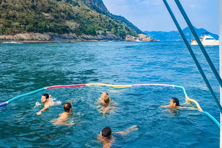 Swim stop during Rio catamaran sailboat private tour, guests in ocean with noodles near lush coastline