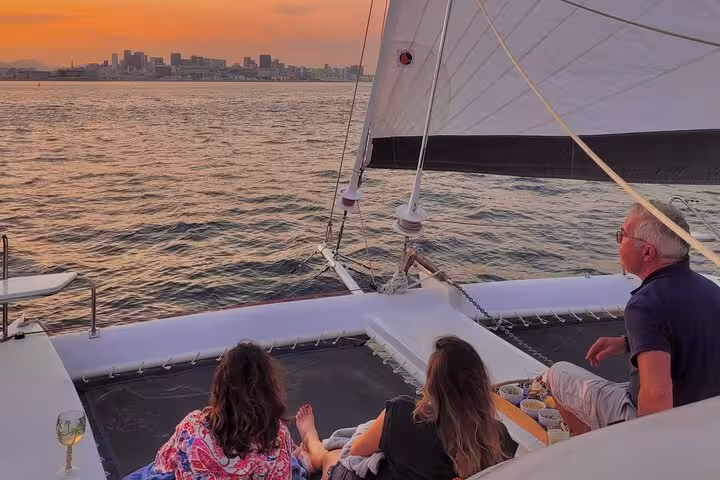 Sunset views from a private Rio catamaran with open bar and BBQ, guests relaxing on deck in Guanabara Bay