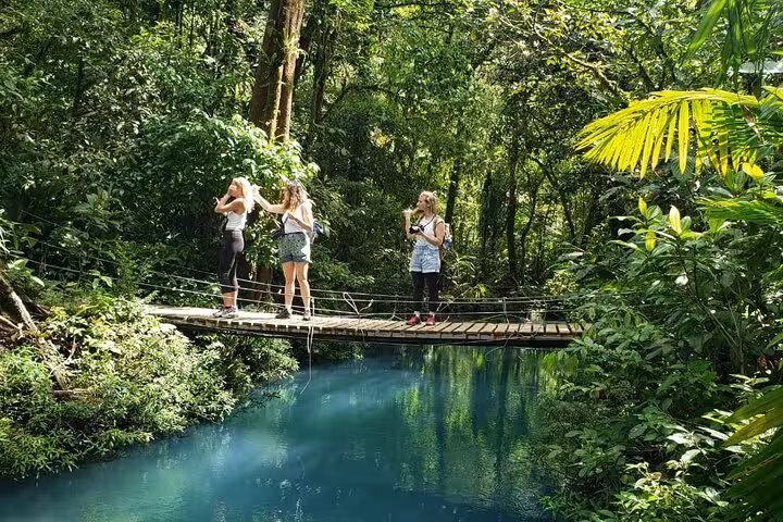 Group of hikers capturing memories on a wooden bridge over the enchanting blue river in Rio Celeste rainforest.