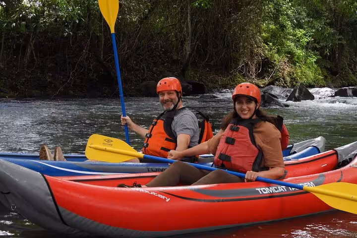 Two people in red kayaks enjoy a guided adventure on the scenic Río Celeste, surrounded by lush greenery.