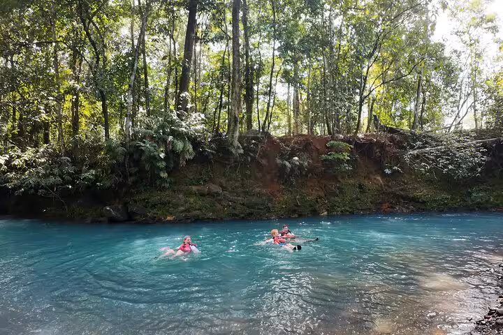 Visitors enjoying a swim in the turquoise waters of Río Celeste surrounded by lush rainforest.