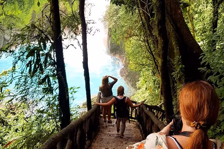 Hikers descend lush forest steps towards the vibrant blue waters of Rio Celeste on an immersive nature hike.