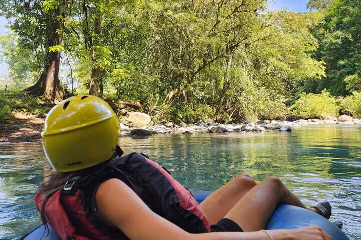 Person relaxing on a tube in Rio Celeste, surrounded by lush greenery on a full-day hiking and tubing tour.