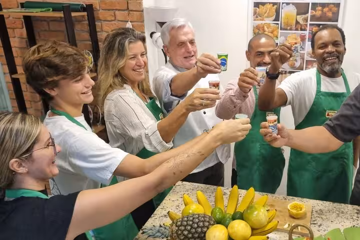 A joyful group of people in aprons toasting with caipirinhas at Rio's cooking fiesta, surrounded by tropical fruits.