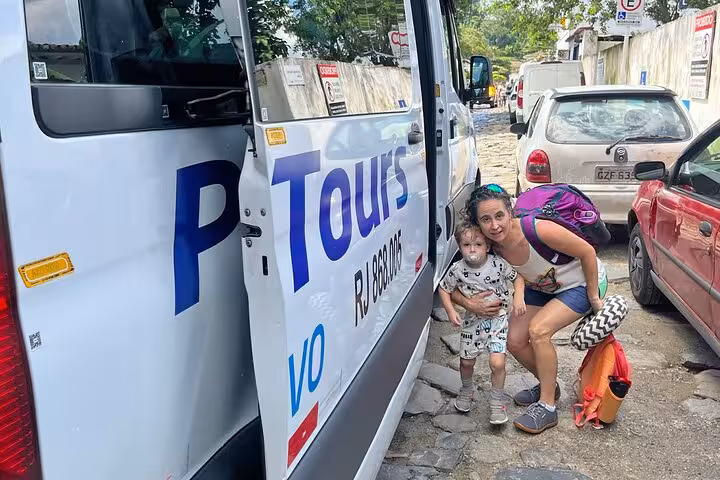 Mother and child ready for Rio de Janeiro to Paraty shared transfer beside a tour van on a sunny day.