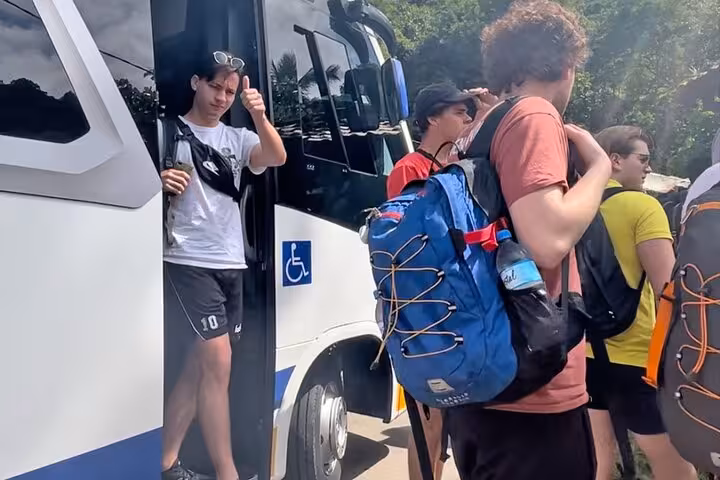 Travelers with backpacks disembark a shuttle bus in lush surroundings at Ilha Grande transfer point.