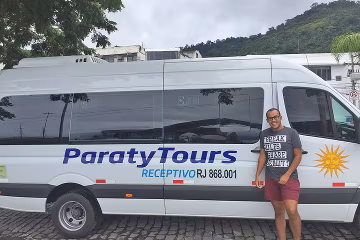 Man posing next to Paraty Tours shuttle, offering reliable transfers from Rio de Janeiro to Ilha Grande.