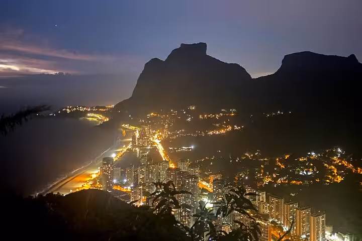 City lights illuminate Rio de Janeiro's coastline as dawn breaks over the iconic Two Brothers peaks.