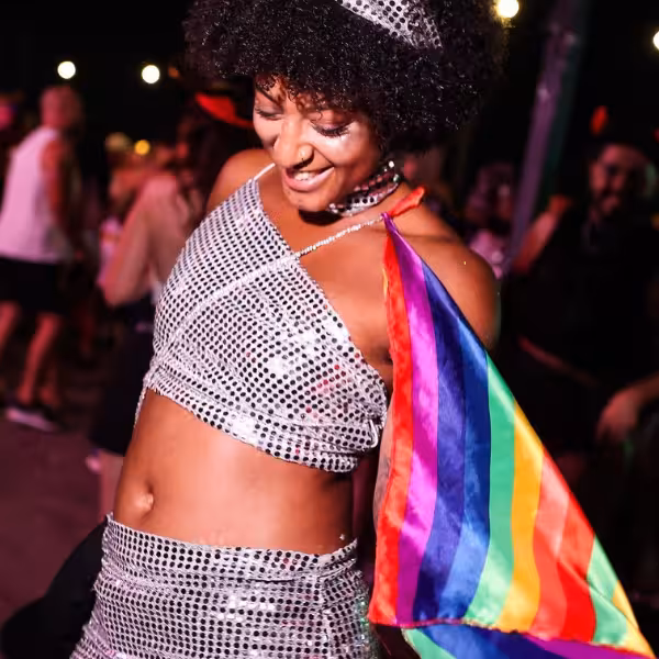 Vibrant Rio Gay Nightlife Experience with Samba, featuring a joyful dancer in sparkling attire holding a rainbow flag.