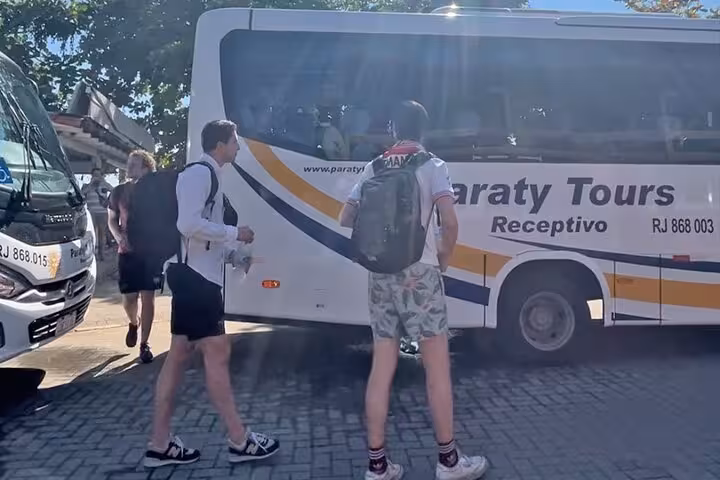 Passengers with backpacks approach a Paraty Tours shuttle bus for the Rio to Ilha Grande transfer.