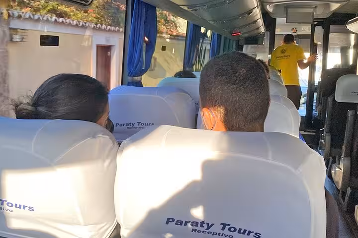 Tourists seated on a Paraty Tours bus, heading from Rio de Janeiro to Ilha Grande, highlighting travel comfort and service.
