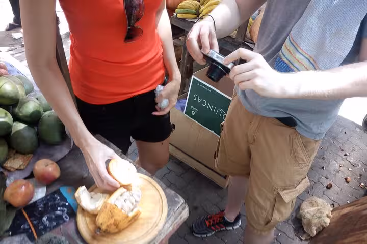 Visitors photographing exotic cacao fruit at a vibrant Rio market during a guided tropical fruit tasting tour.