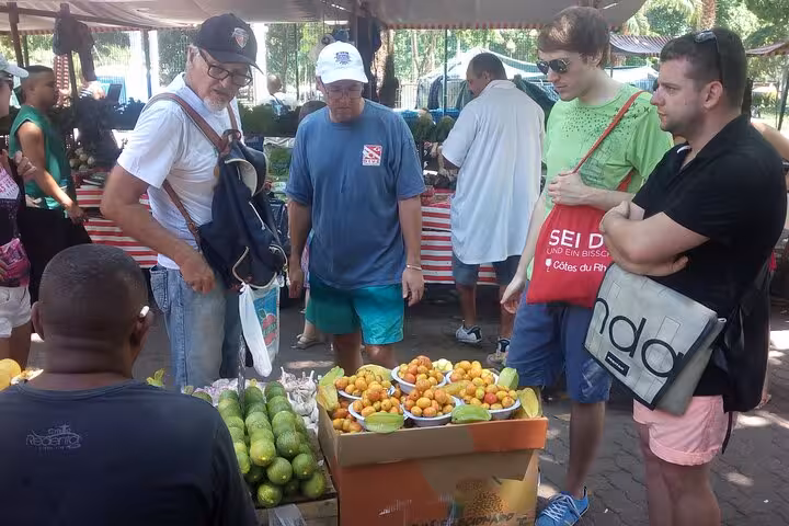 Tourists explore a vibrant Rio market, engaging with fresh tropical fruits for an authentic tasting experience.