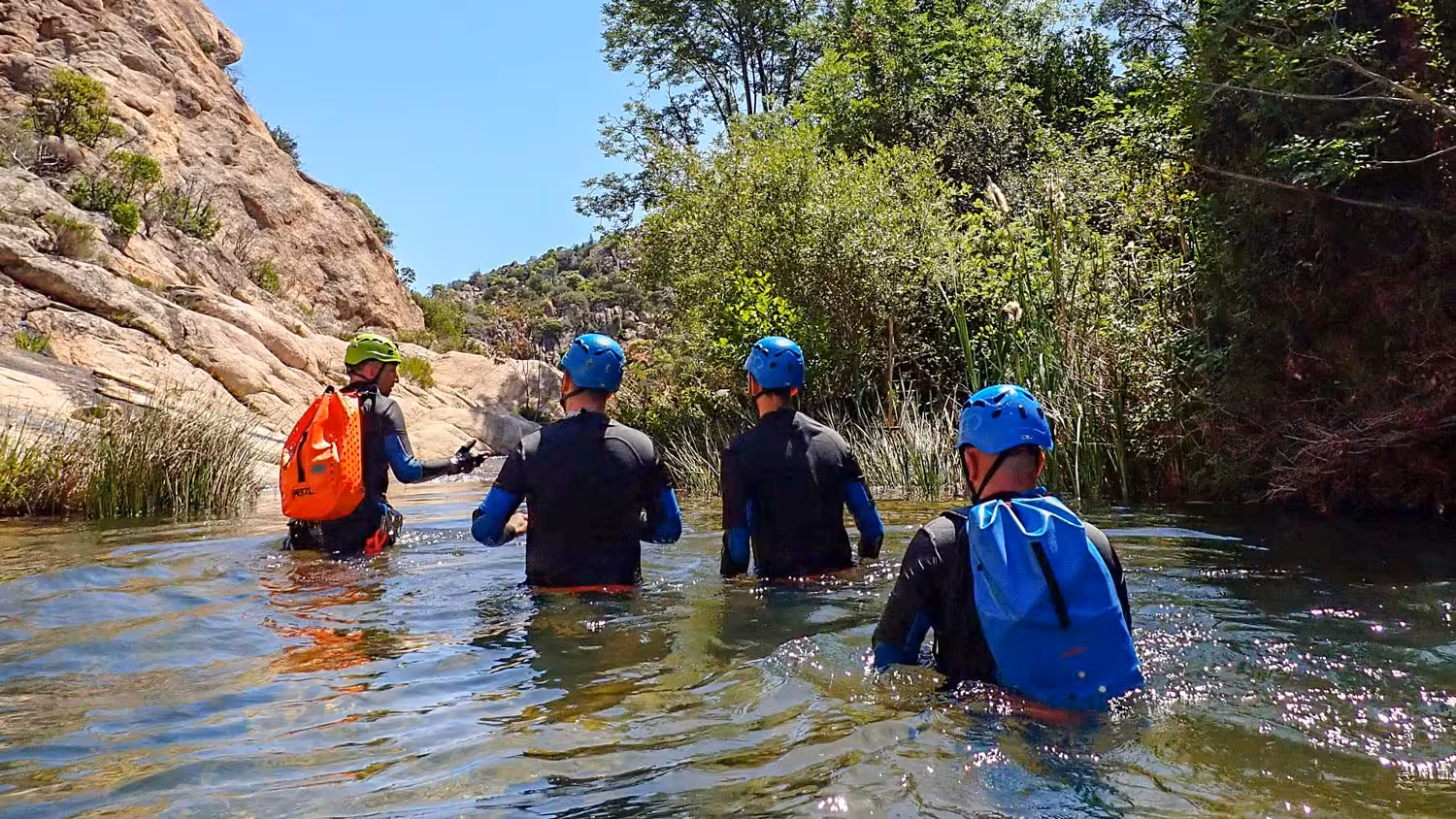 Adventurers in wetsuits canyoning through Rio Pitrisconi's clear waters, surrounded by lush greenery and rocky cliffs.