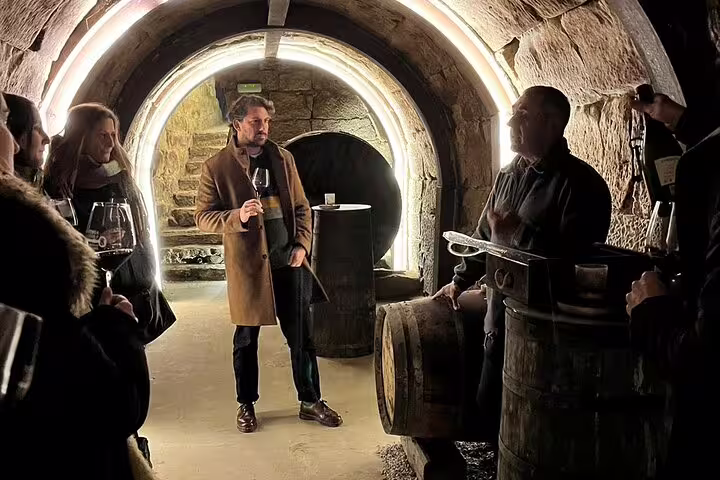 Tour group enjoying wine tasting in a historic Rioja winery cellar, surrounded by rustic stone arches and barrels.