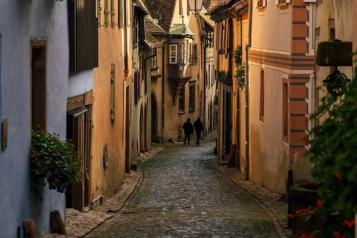 Narrow cobblestone alley with historic half-timbered buildings in Riquewihr, Alsace, two silhouetted figures walking