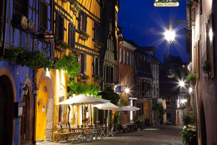 Illuminated half-timbered buildings and outdoor cafe along cobblestone street in Riquewihr at night