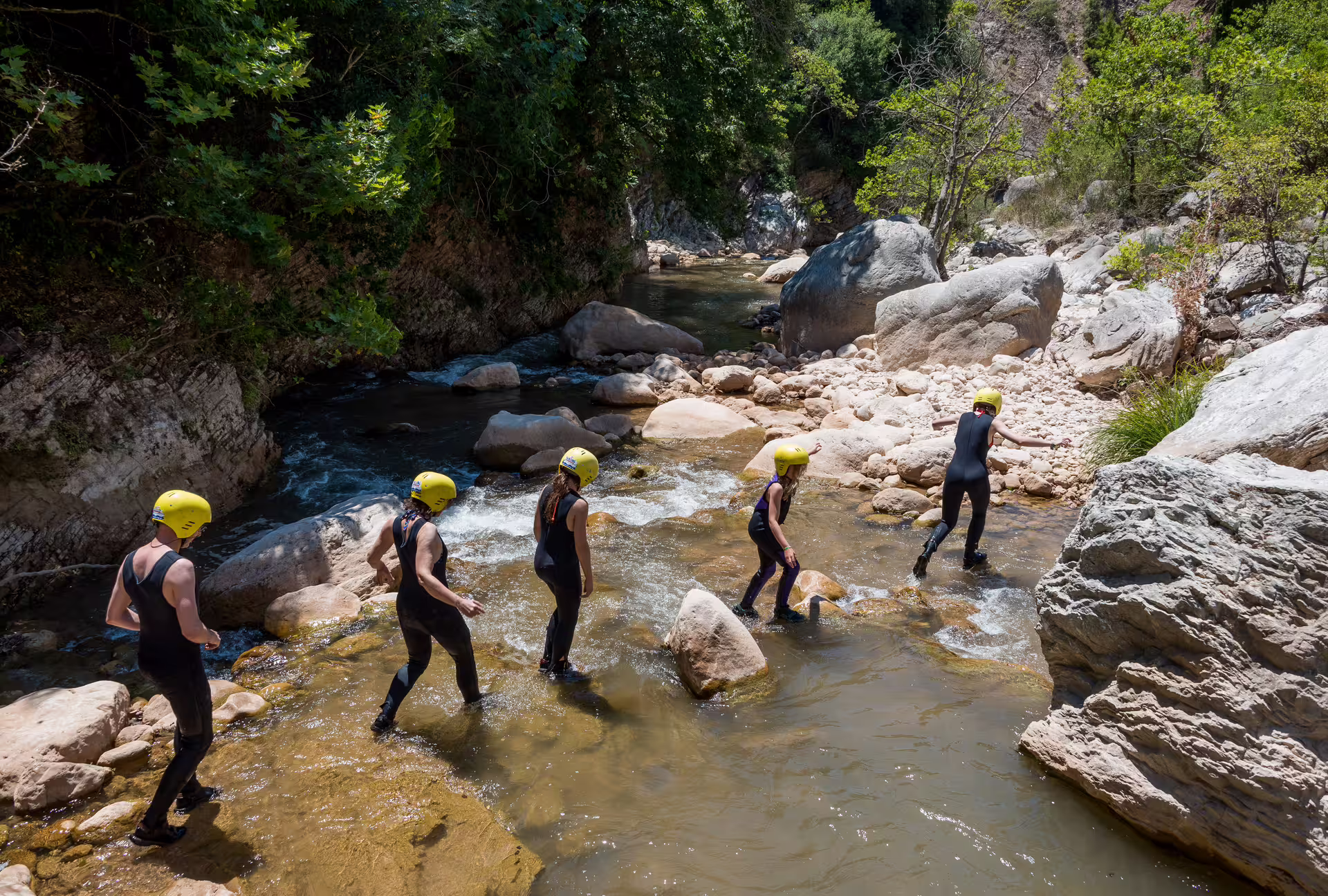 Guided River Trekking Neda group wading through shallow canyon stream with helmets and wetsuits