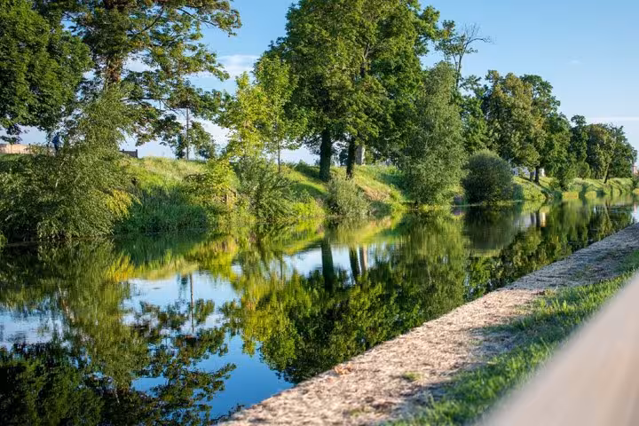 Calm canal with lush green tree reflections on a sunny day in Roanne, France