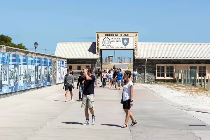 Tourists exploring the historic entrance of Robben Island under a clear blue sky on a guided full day tour.