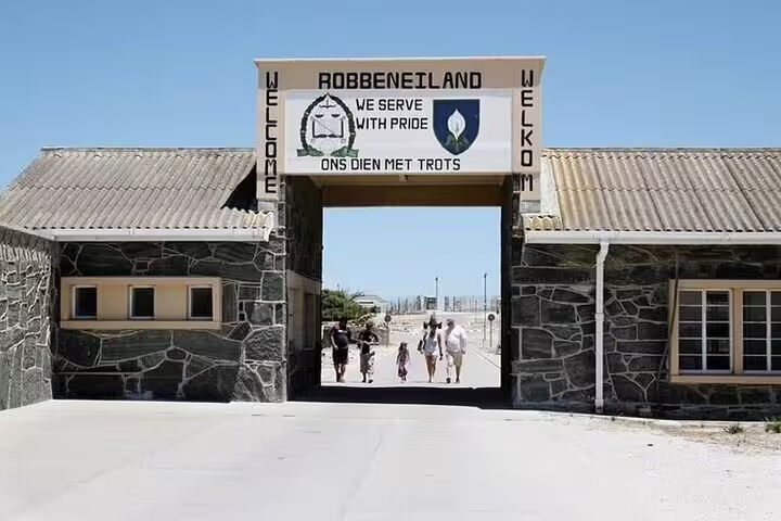 Entrance to Robben Island with visitors walking through the historic gateway under a clear blue sky.
