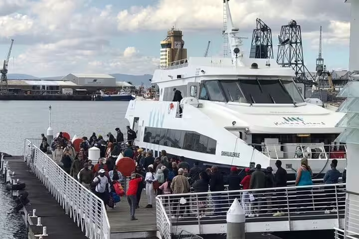 Visitors boarding a ferry to Robben Island from Cape Town harbor, with industrial docks in the background.