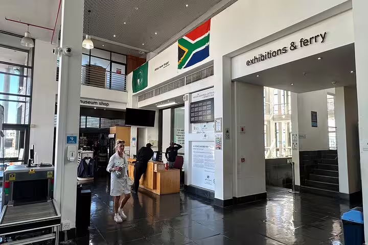 Interior of Robben Island Museum featuring exhibitions, ferry access, and South African flag.