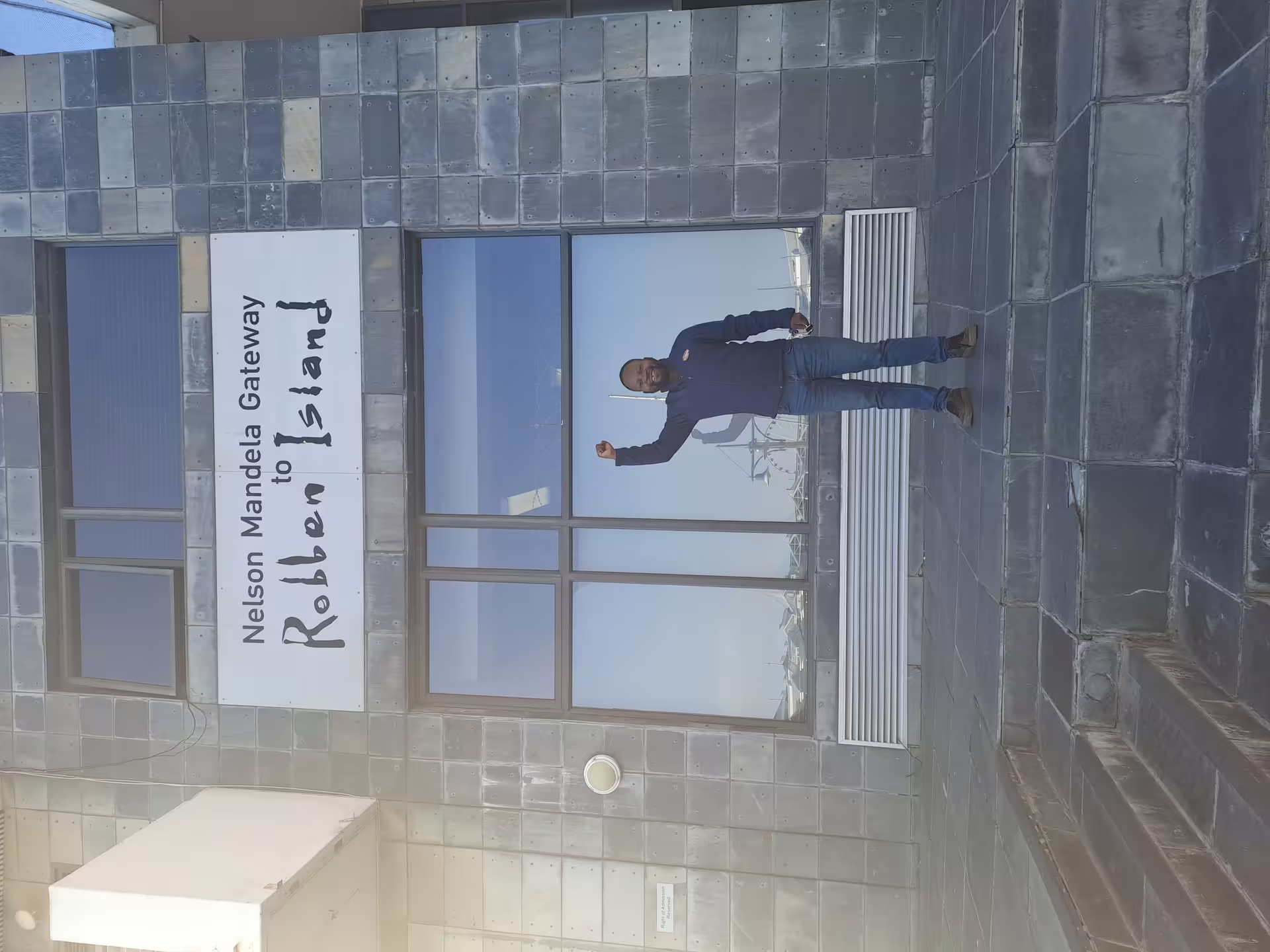 Visitor standing at the Nelson Mandela Gateway to Robben Island Museum, ready for a ferry tour adventure.