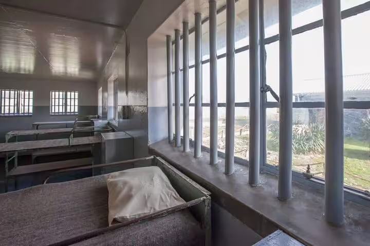 Interior of a cell block on Robben Island, showcasing historical prison bars and beds during the guided tour.