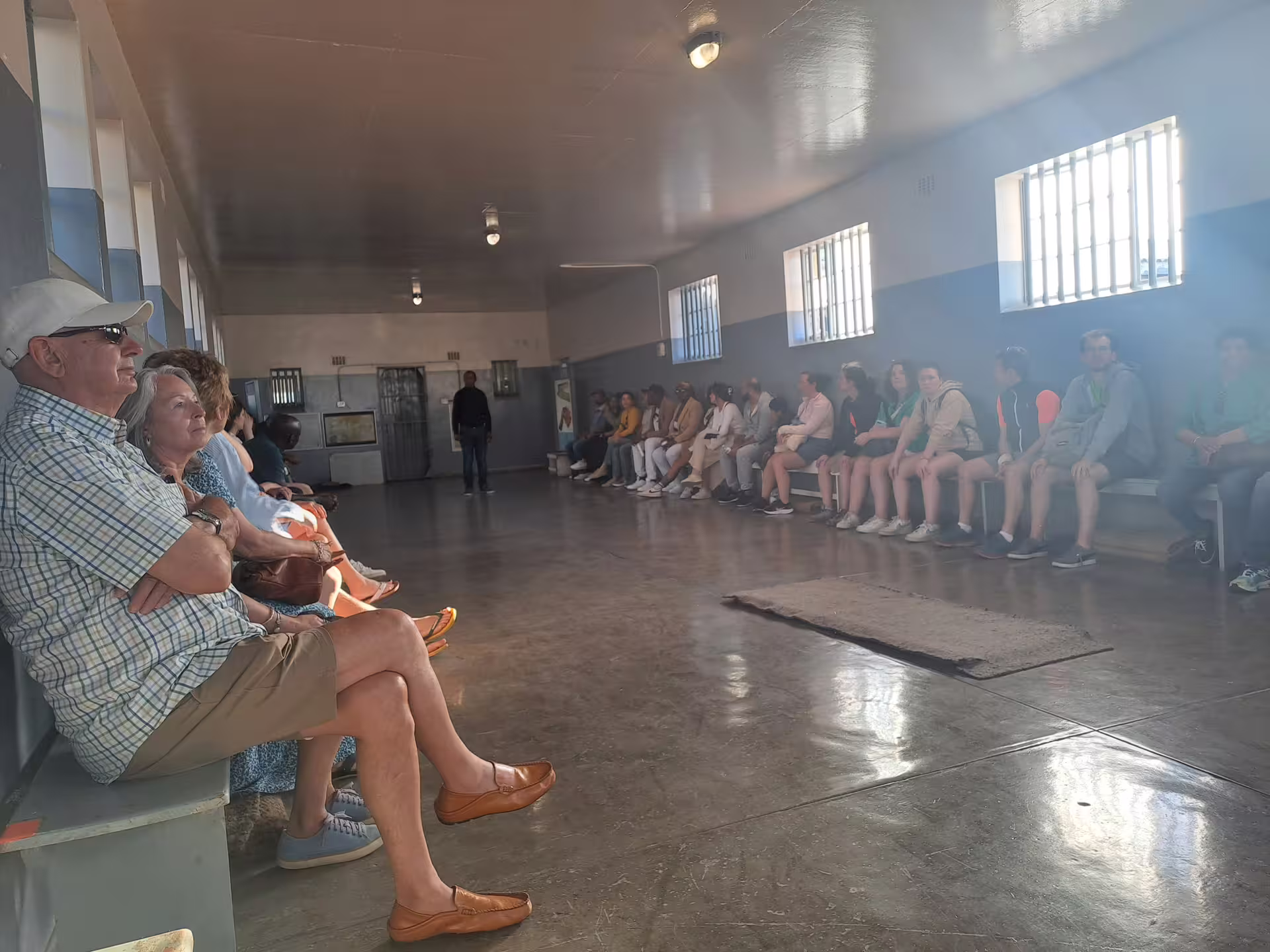 Visitors seated inside Robben Island prison cell on a guided tour, part of Cape Town's historical itinerary.