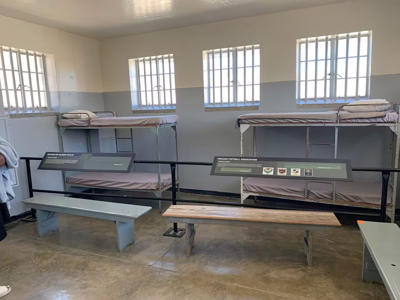 Interior of a Robben Island prison cell with bunk beds and historical displays, showcasing the island's rich history.