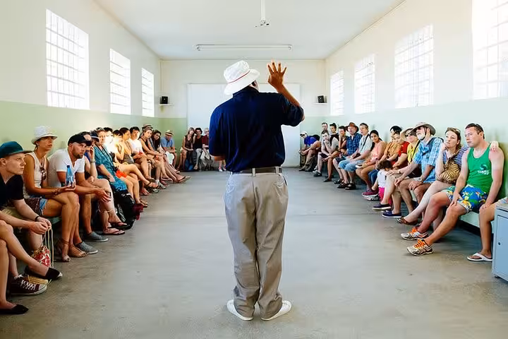 Tour guide engaging visitors in historical Robben Island prison room, enhancing cultural experience near Table Mountain.