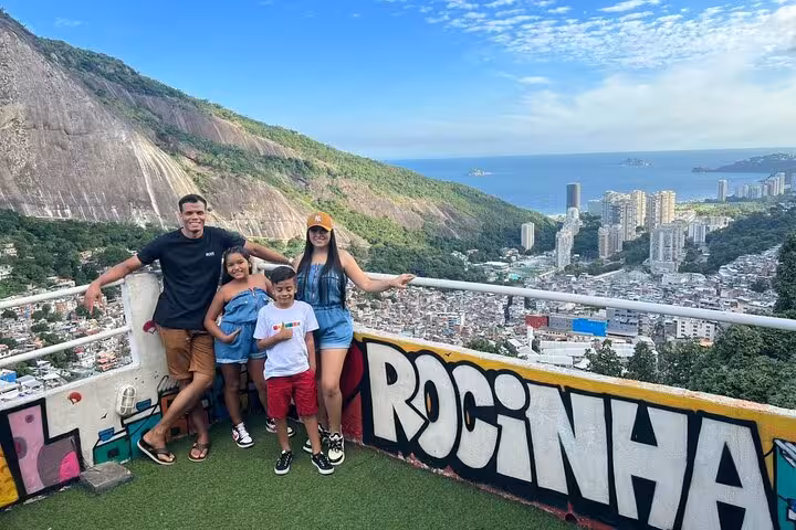 Family posing with a panoramic view of Rocinha favela and Rio de Janeiro coastline, showcasing vibrant street art.