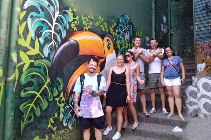 Group of tourists posing by vibrant toucan mural during Rocinha favela tour, showcasing local art and culture.