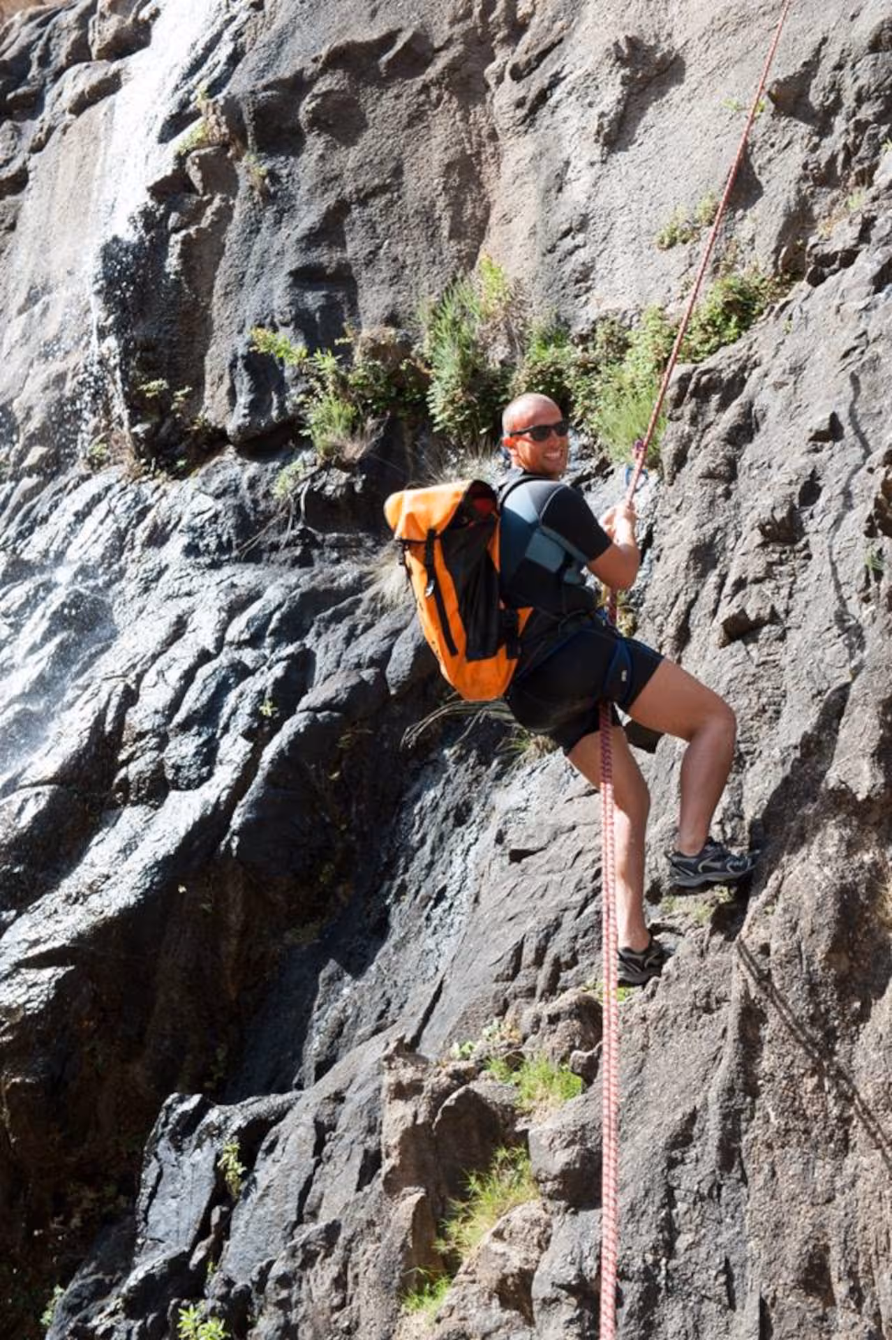 Climber with orange backpack ascends rocky cliff in Fuili Canyon, enjoying outdoor adventure in Cala Gonone.
