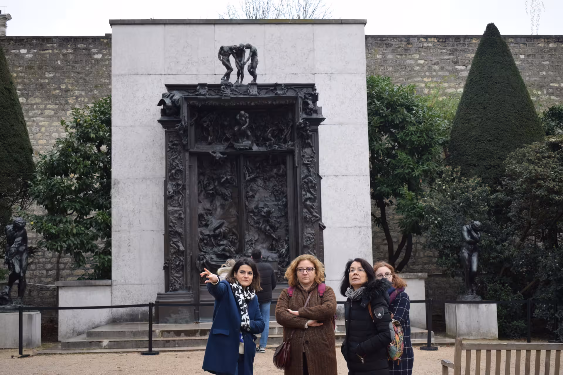 Tour guide pointing at Rodin's Gates of Hell bronze sculpture in Musée Rodin garden, Paris