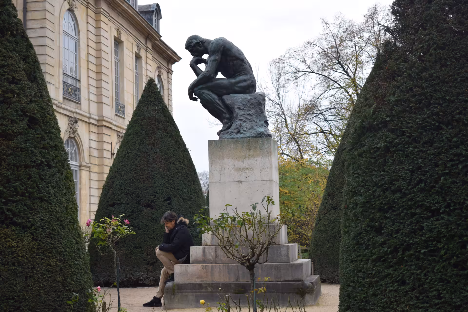 The Thinker bronze sculpture by Rodin in garden of Rodin Museum Paris with visitor seated at base