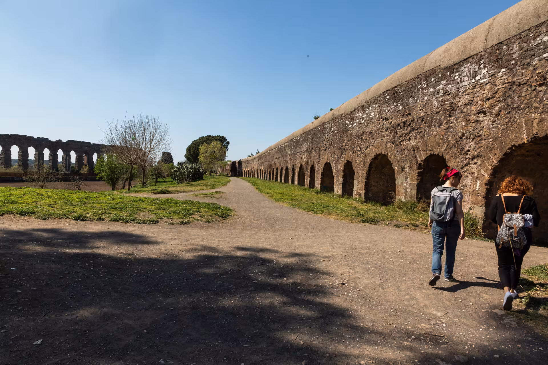 Tourists walking along a historic Roman aqueduct in the scenic Caffarella Valley.