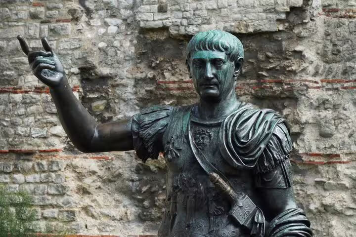 Bronze Roman emperor statue with raised hand against ancient stone wall in London